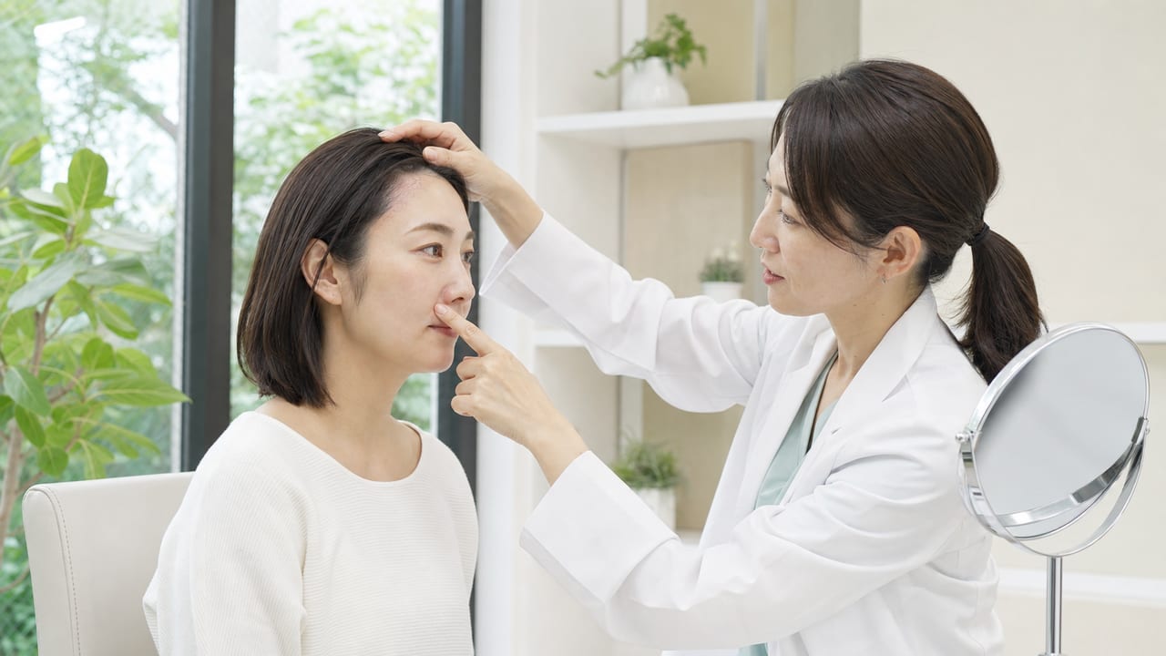 皮膚科医が成人女性の髪の生え際と鼻のわきにみられる脂漏性皮膚炎を診察する様子
